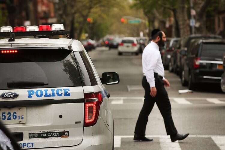 A Hassidic man walks by a police car in a Jewish Orthodox neighborhood in Brooklyn