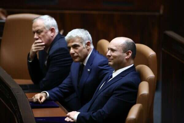 Prime Minister Naftali Bennett, right, sits in the Knesset plenum on Sunday, June 13, 2021, with Blue and White leader Benny Gantz, left, and Yesh Atid leader and Prime MInister-designate Yair Lapid