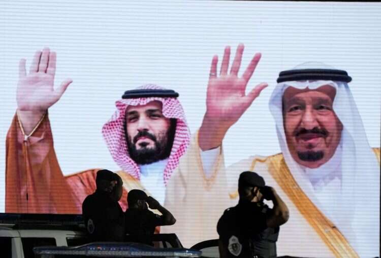 Saudi special forces salute in front of a screen displaying images Saudi King Salman and Crown Prince Mohammed bin Salman in Mecca, July 3, 2022