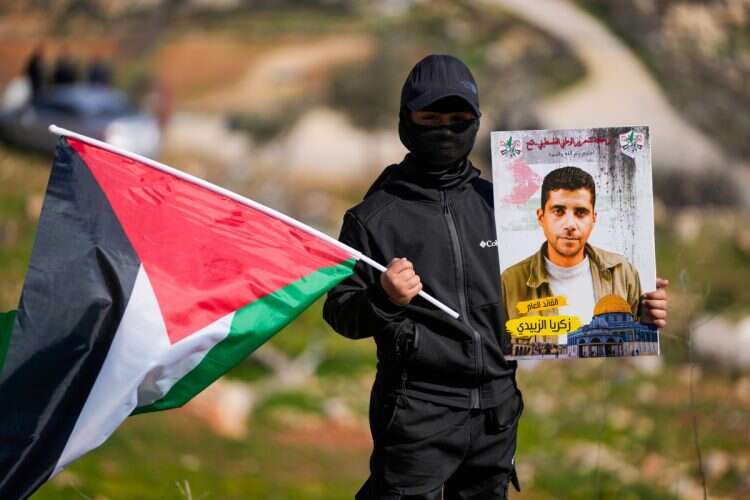 A young boy holds a Palestinian flag and a photograph of Palestinian terrorist Zakaria Al-Zubaidi outside the Israeli Ofer prison in the West Bank city of Beitunia, on Thursday, Jan. 30, 2025